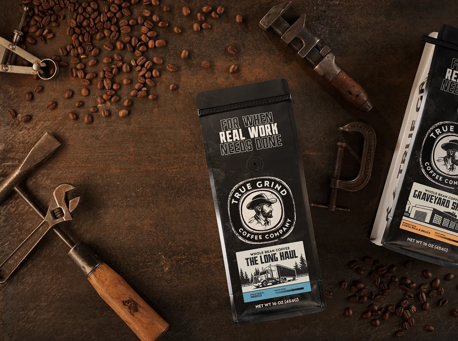 True Grind Coffee bags laid out on a workbench with various woodworking tools and scattered coffee beans.